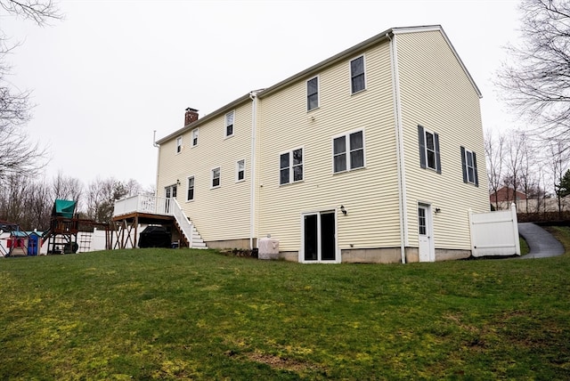 back of property with a playground, a wooden deck, and a lawn