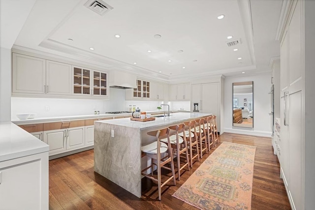 kitchen with a raised ceiling, visible vents, wood finished floors, gas cooktop, and an island with sink