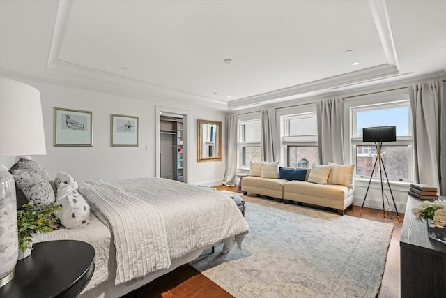 bedroom featuring ornamental molding, a tray ceiling, wood finished floors, and baseboards