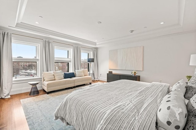 bedroom featuring ornamental molding, light wood-type flooring, and a raised ceiling