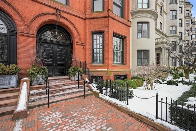 snow covered property entrance with brick siding and fence