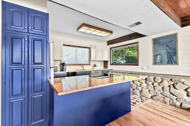 kitchen with backsplash, light hardwood / wood-style flooring, light stone counters, sink, and blue cabinets