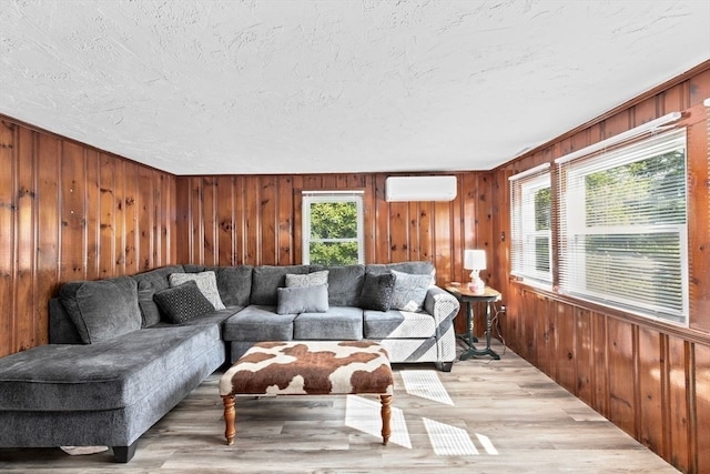 living room with a textured ceiling, wood walls, an AC wall unit, and light hardwood / wood-style floors