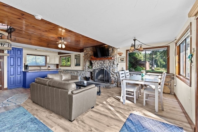 living room with ceiling fan, a stone fireplace, light wood-type flooring, and wooden ceiling