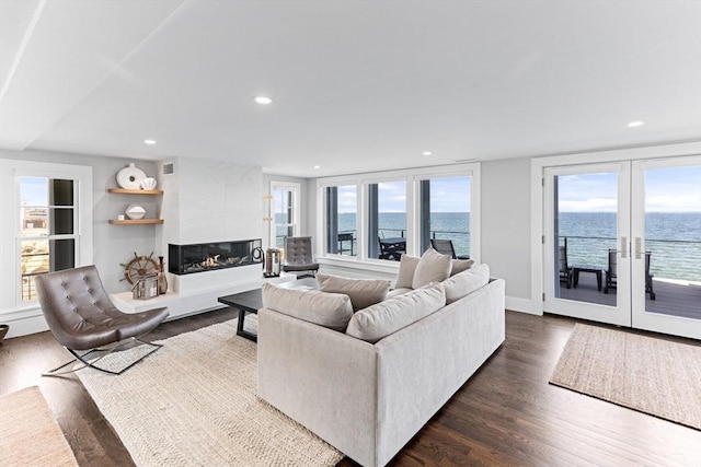 living room featuring dark wood-style flooring, recessed lighting, french doors, a water view, and a premium fireplace