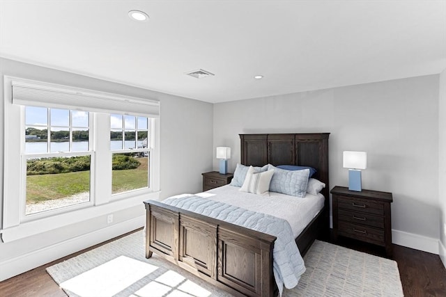 bedroom with a water view, visible vents, baseboards, and wood finished floors