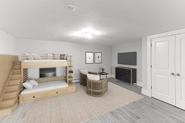 bedroom with a closet, a baseboard radiator, baseboards, and wood finish floors