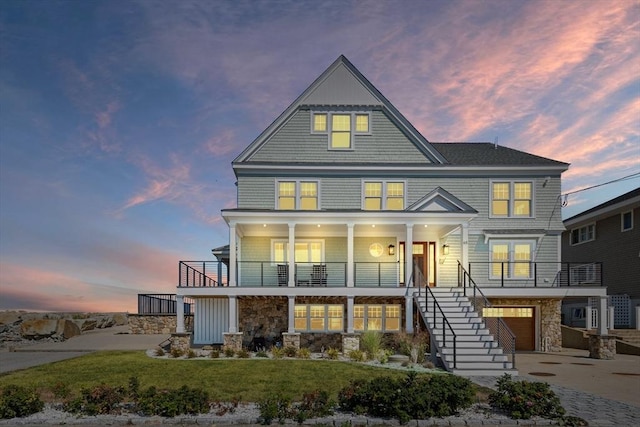 beach home with a lawn, stairway, stone siding, an attached garage, and concrete driveway