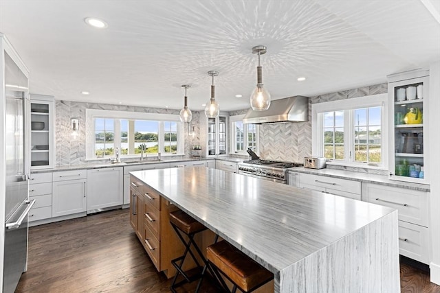 kitchen featuring dishwasher, wall chimney range hood, stainless steel gas range, a spacious island, and decorative backsplash