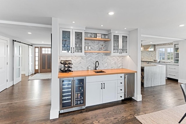 bar featuring tasteful backsplash, indoor wet bar, a barn door, wine cooler, and a sink