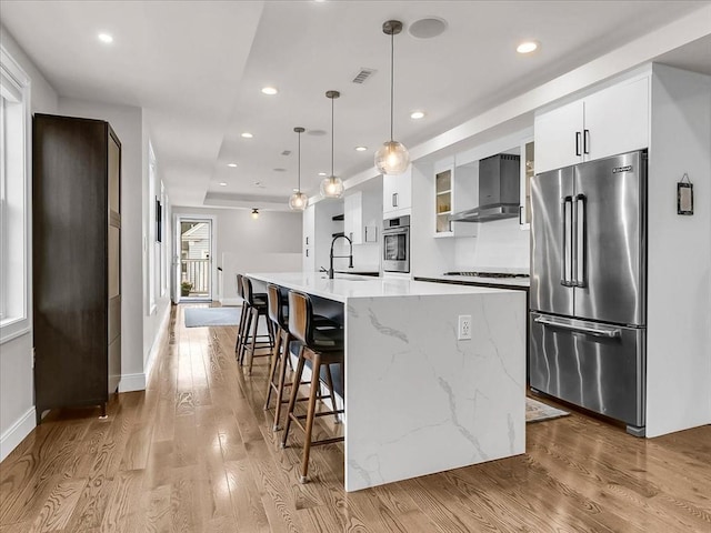 72-74 Grafton St Unit 2, Arlington, MA 02474 - kitchen with stainless steel appliances, wall chimney exhaust hood, a sink, white cabinetry, and light wood finished floors