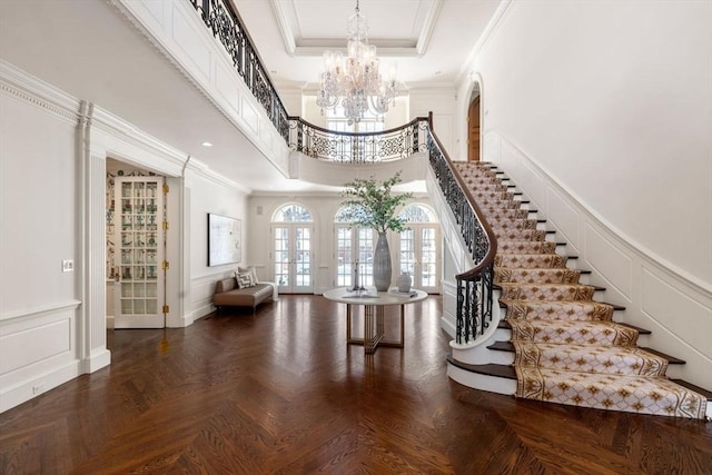 entrance foyer featuring crown molding, parquet flooring, a notable chandelier, and french doors