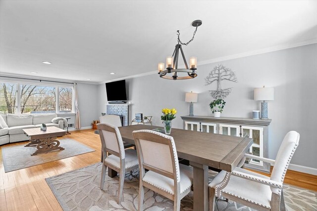 dining area featuring a fireplace, baseboards, light wood-type flooring, and ornamental molding