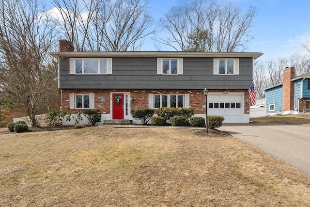 colonial inspired home with driveway, an attached garage, a front yard, brick siding, and a chimney