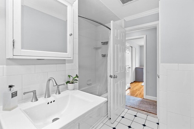 full bathroom featuring tile patterned floors, tile walls, crown molding, and a sink