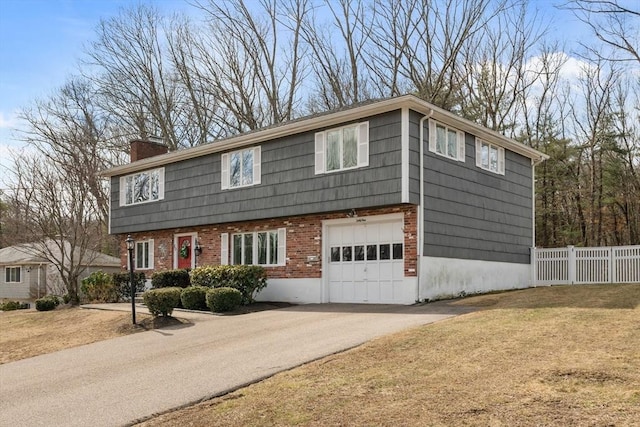 colonial inspired home featuring aphalt driveway, fence, an attached garage, brick siding, and a chimney