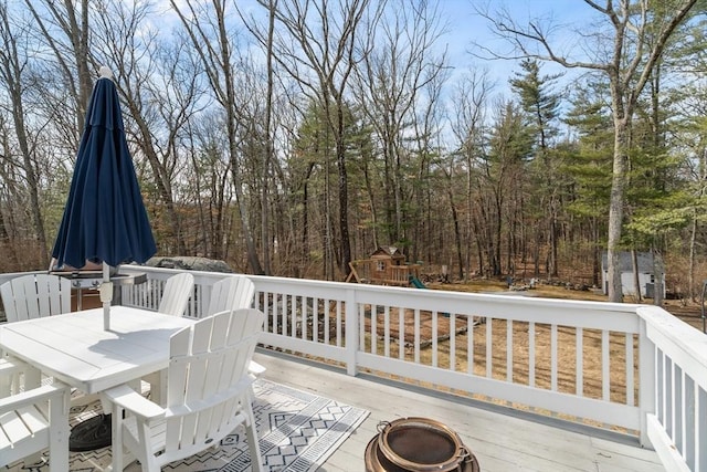 wooden terrace featuring outdoor dining space, a fire pit, and a playground