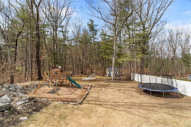 view of yard with a forest view, an outbuilding, a trampoline, and a playground