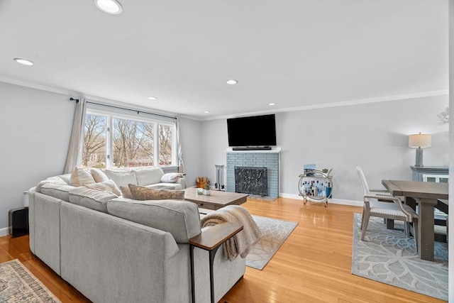 living room featuring a brick fireplace, baseboards, light wood-type flooring, ornamental molding, and recessed lighting