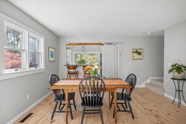 dining room with light wood-type flooring, baseboards, and stairs