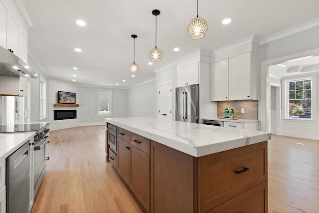 kitchen with appliances with stainless steel finishes, pendant lighting, light stone counters, a spacious island, and white cabinets