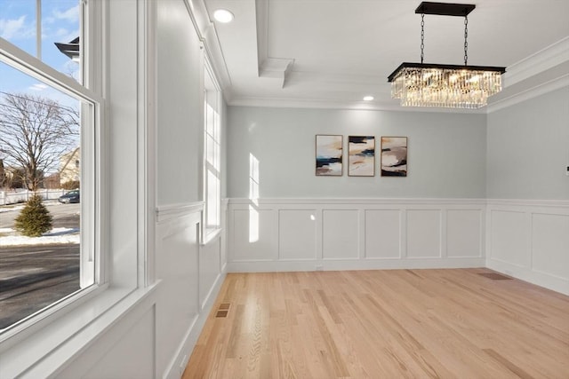 unfurnished dining area featuring a healthy amount of sunlight, light hardwood / wood-style floors, an inviting chandelier, and crown molding