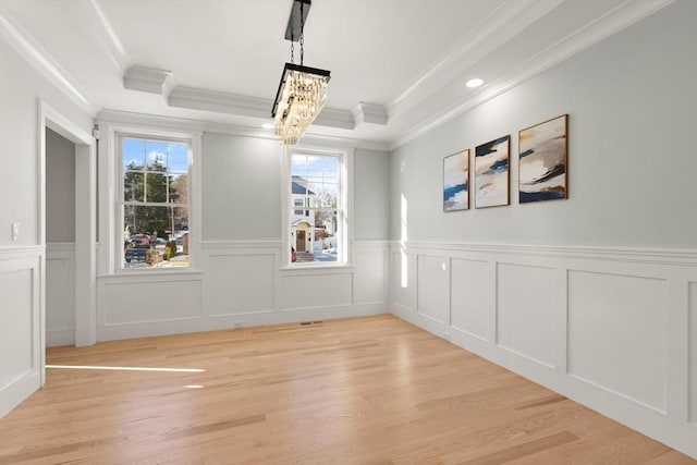 unfurnished room with ornamental molding, a tray ceiling, a chandelier, and light hardwood / wood-style flooring