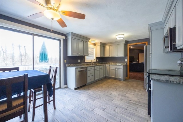 kitchen with stainless steel appliances, gray cabinets, a ceiling fan, a sink, and dark countertops