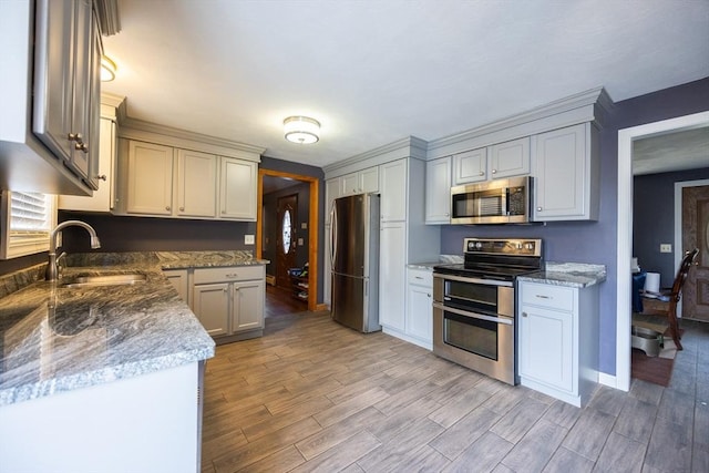 kitchen featuring appliances with stainless steel finishes, a sink, light wood-style flooring, and baseboards