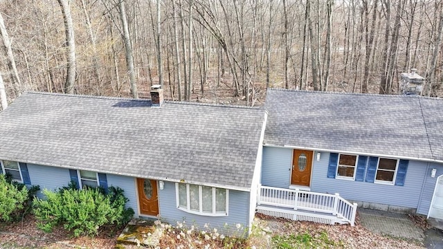 view of front of home with roof with shingles, a chimney, and a porch