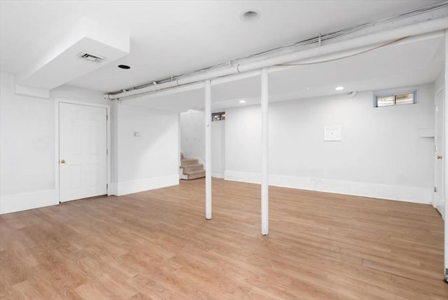 below grade area featuring visible vents, baseboards, light wood finished floors, and stairs