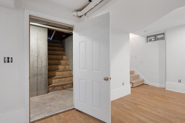 finished basement featuring light wood finished floors, baseboards, and stairway