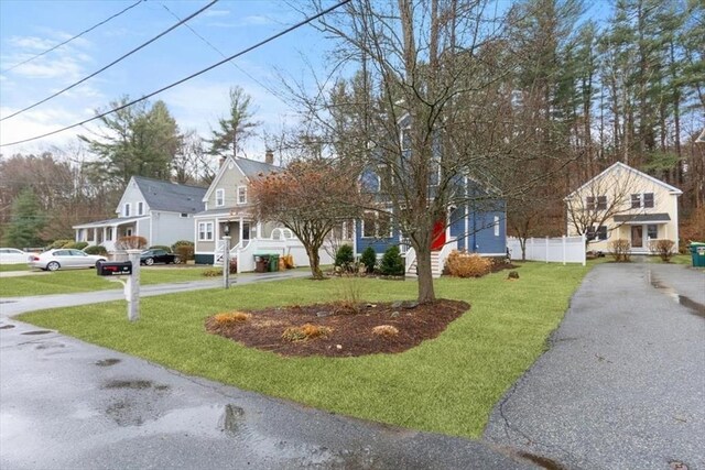 view of front of house with aphalt driveway, fence, and a front lawn