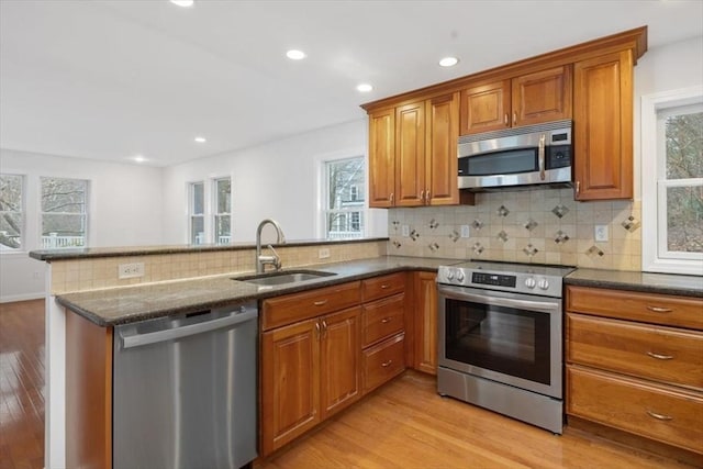 kitchen featuring dark stone countertops, a peninsula, brown cabinets, appliances with stainless steel finishes, and a sink