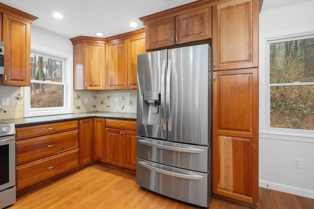 kitchen with brown cabinets, appliances with stainless steel finishes, decorative backsplash, and light wood-type flooring