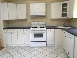 kitchen with white appliances, exhaust hood, sink, light tile patterned floors, and white cabinetry