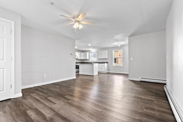 unfurnished living room featuring a baseboard heating unit, a ceiling fan, baseboards, and dark wood-style floors