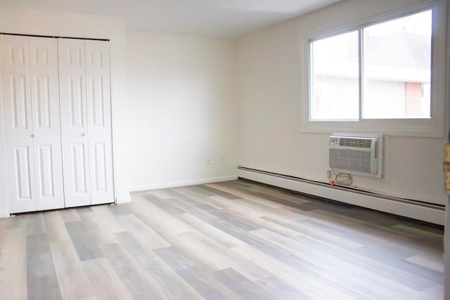 unfurnished bedroom with a wall unit AC, baseboards, baseboard heating, a closet, and light wood finished floors