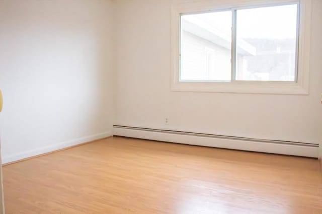 empty room featuring a baseboard radiator, baseboards, and wood finished floors