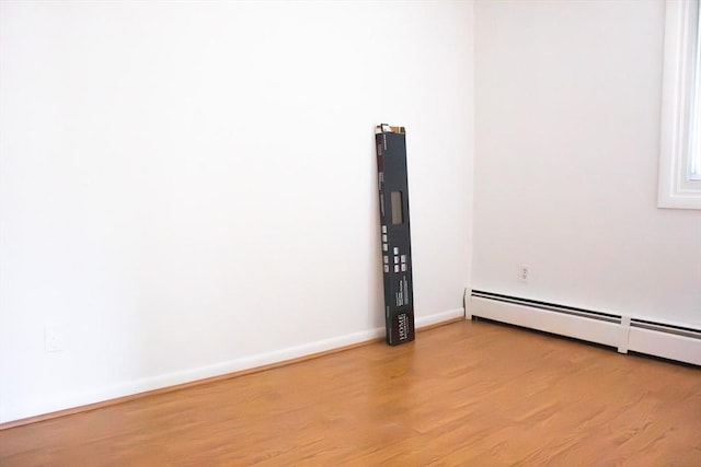 unfurnished room featuring baseboard heating, wood finished floors, and baseboards