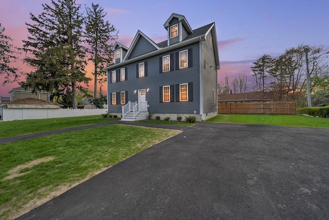 colonial house with a lawn, aphalt driveway, and fence