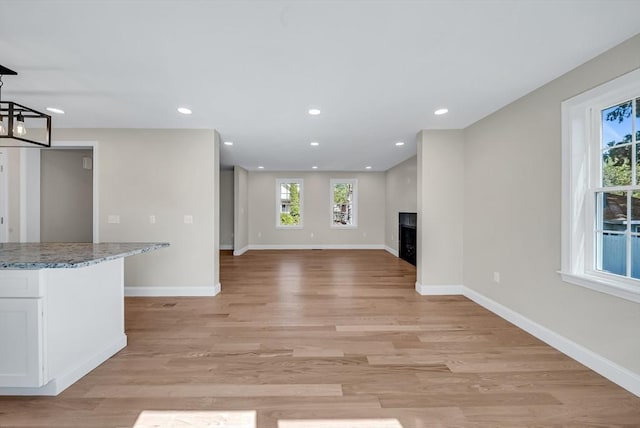 unfurnished living room featuring baseboards, a fireplace, light wood-style flooring, and recessed lighting