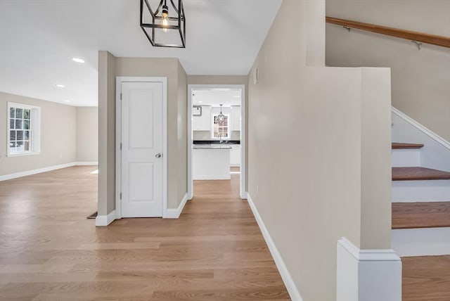 corridor with light wood finished floors, stairway, baseboards, recessed lighting, and a sink