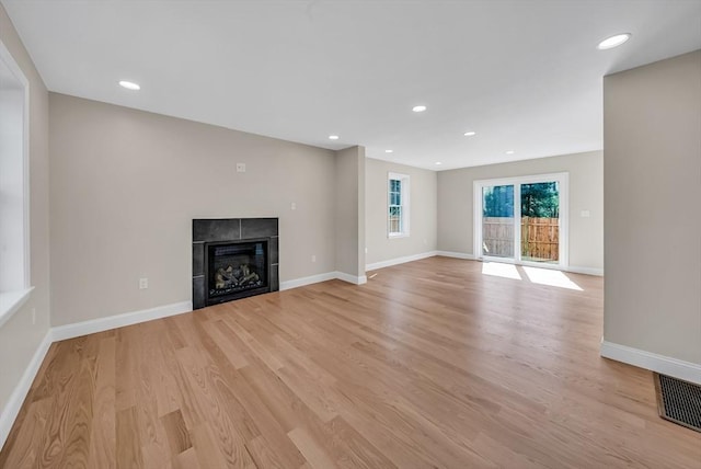 unfurnished living room featuring light wood-style flooring, baseboards, a tile fireplace, and recessed lighting