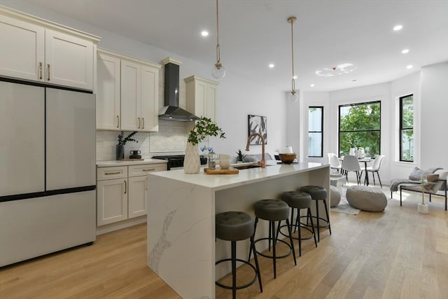 kitchen with wall chimney exhaust hood, white fridge, sink, and a kitchen island with sink