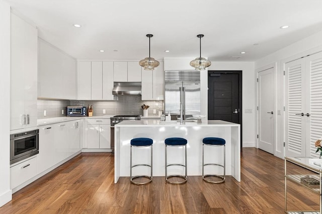 kitchen with high quality appliances, decorative light fixtures, a center island, light countertops, and under cabinet range hood