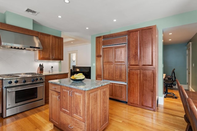 19 Woodbine St Unit B, Newton, MA 02466 - kitchen with high end appliances, wall chimney range hood, light stone counters, a center island, and light wood-style flooring