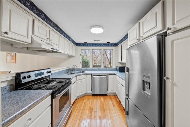 kitchen featuring under cabinet range hood, white cabinets, a sink, light wood finished floors, and appliances with stainless steel finishes