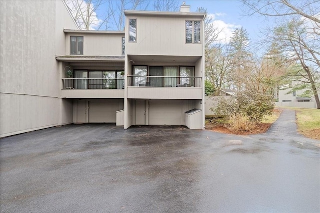 back of property with an attached garage, a chimney, driveway, and a balcony