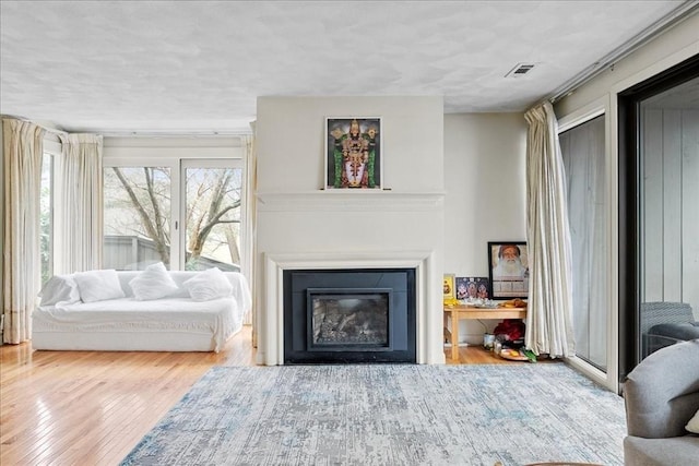 living room featuring visible vents, a glass covered fireplace, and wood finished floors